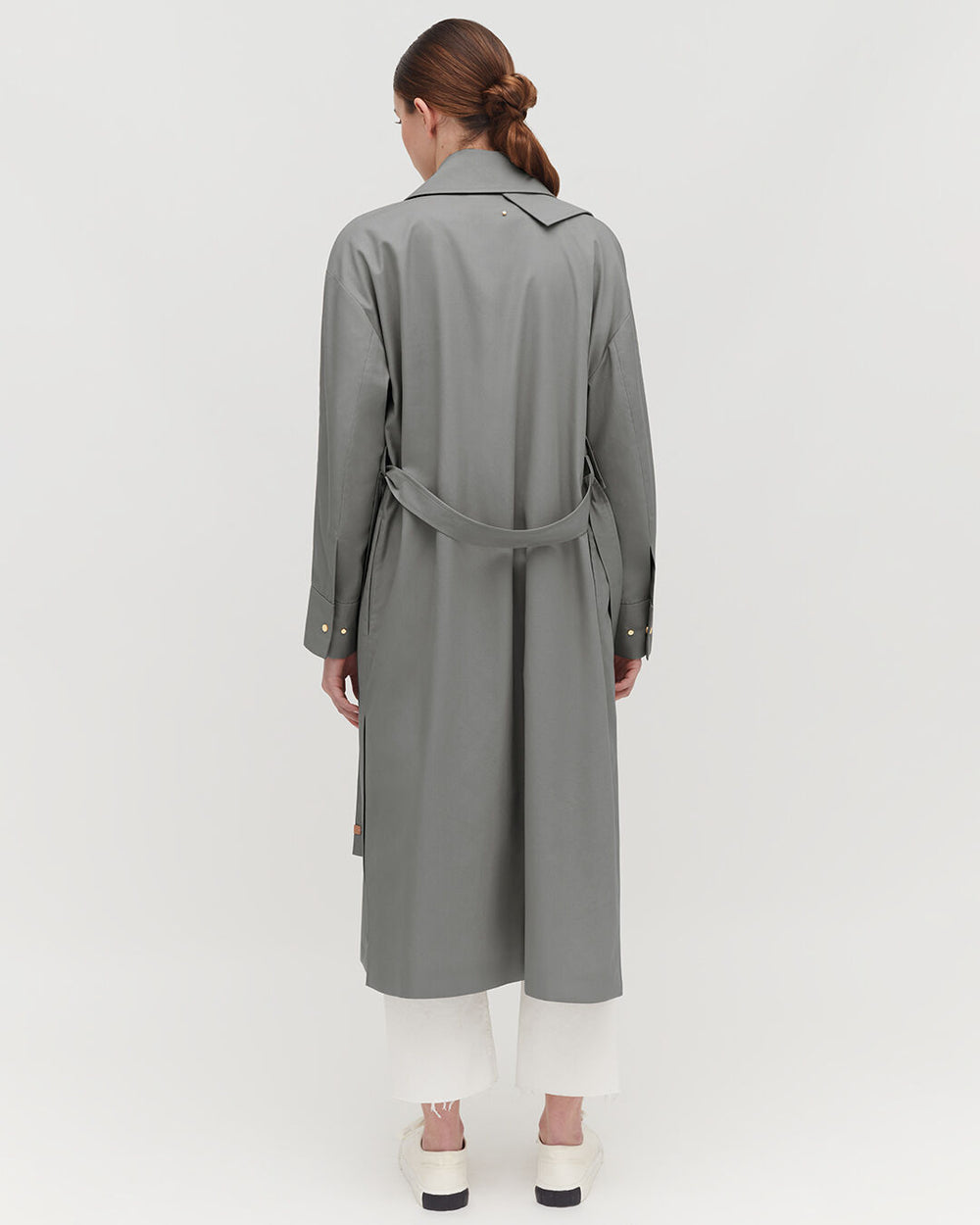 Woman wearing a long coat and trousers, viewed from behind.