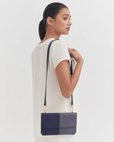 Woman standing with purse on shoulder, looking over her shoulder.