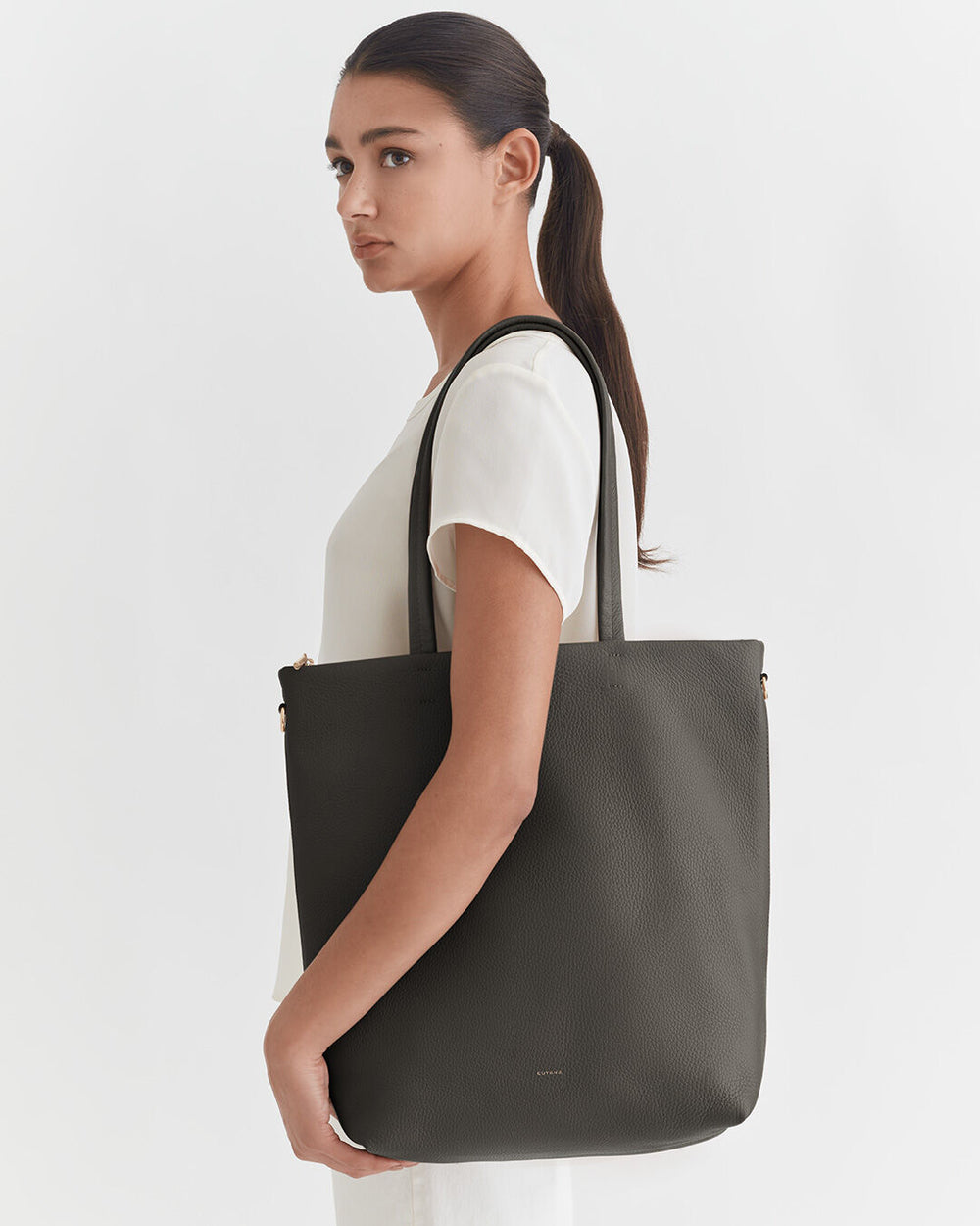 Woman standing sideways holding a large shoulder bag.