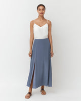Woman in a sleeveless top and long skirt standing against a white background.