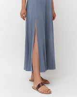Person wearing a long dress with a front slit and sandals, shown from waist down.