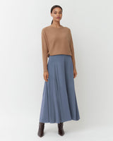 Woman standing in a sweater and long skirt with boots.