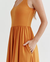 Woman in sleeveless dress holding the fabric near her waist.