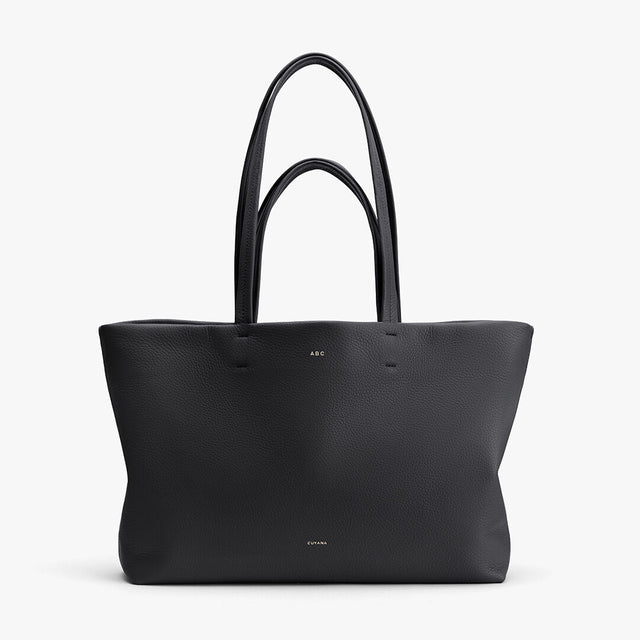 Leather tote bag with two handles standing upright.