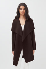 Woman standing in a studio wearing a coat and pants.
