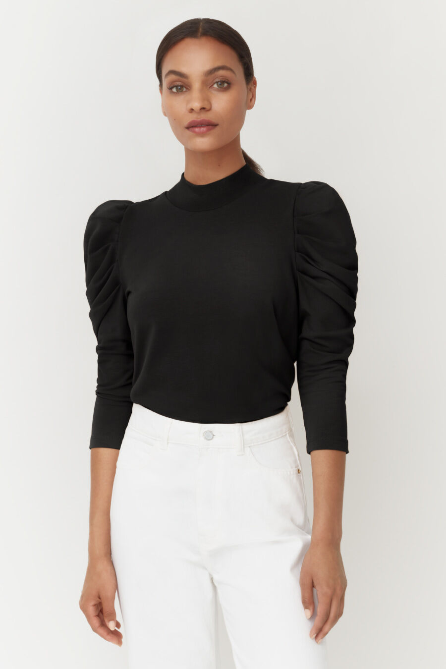 Woman in a turtleneck with puffed sleeves standing straight.