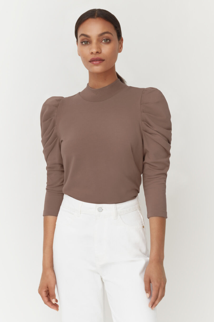 Woman standing in a long-sleeve top and pants, looking at the camera.