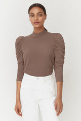 Woman standing in a long-sleeve top and pants, looking at the camera.