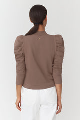 Woman facing away with a ponytail, wearing a top with puffed sleeves.