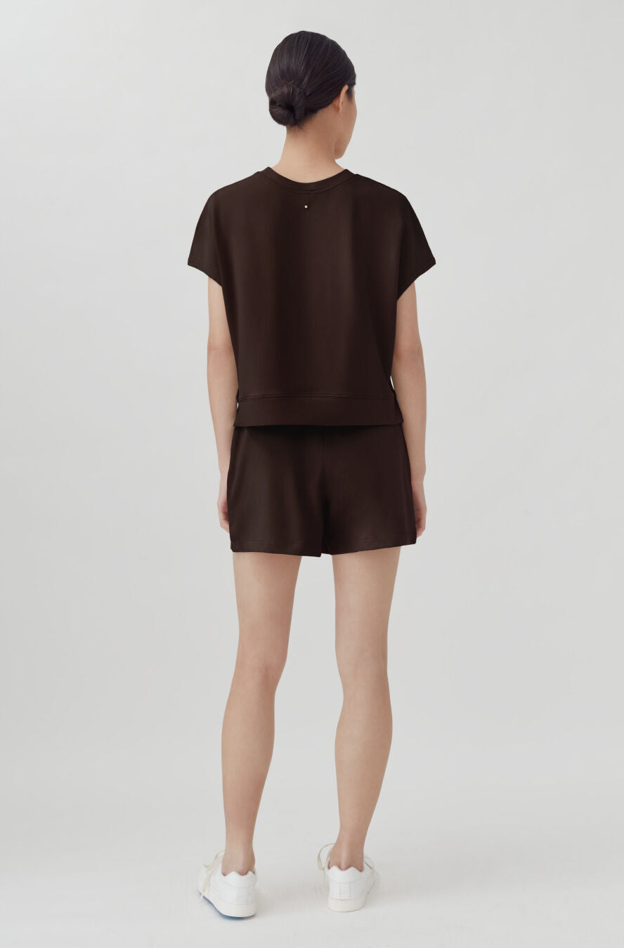 Woman standing with back turned, wearing a short sleeve top and shorts, and sneakers.