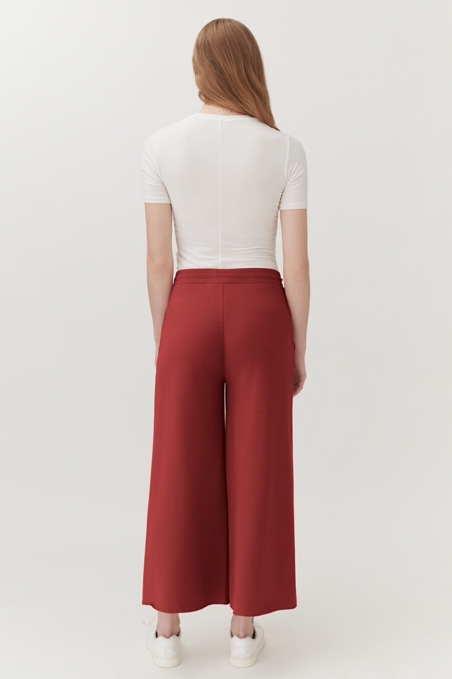 Woman standing facing away, wearing a shirt and wide-legged pants.