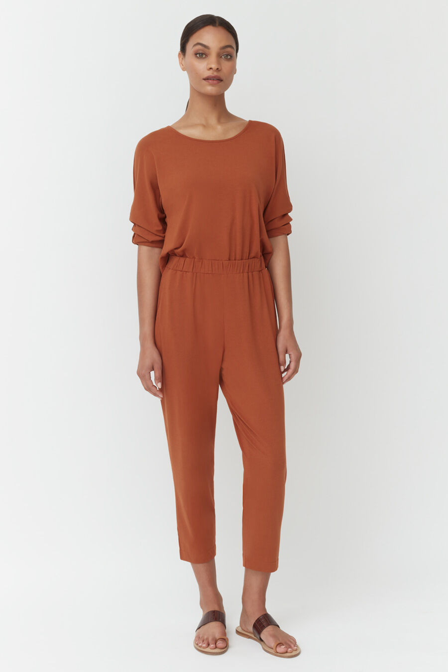 Woman standing in jumpsuit with sandals on plain background
