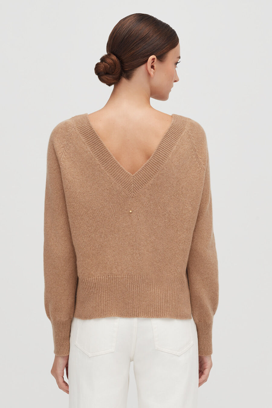Woman in sweater with V-neck back standing with back to camera.