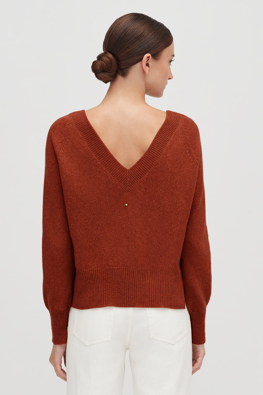 Woman facing away, wearing a V-neck sweater and pants.