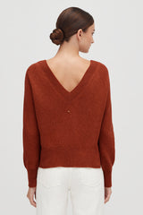 Woman facing away, wearing a V-neck sweater and pants.