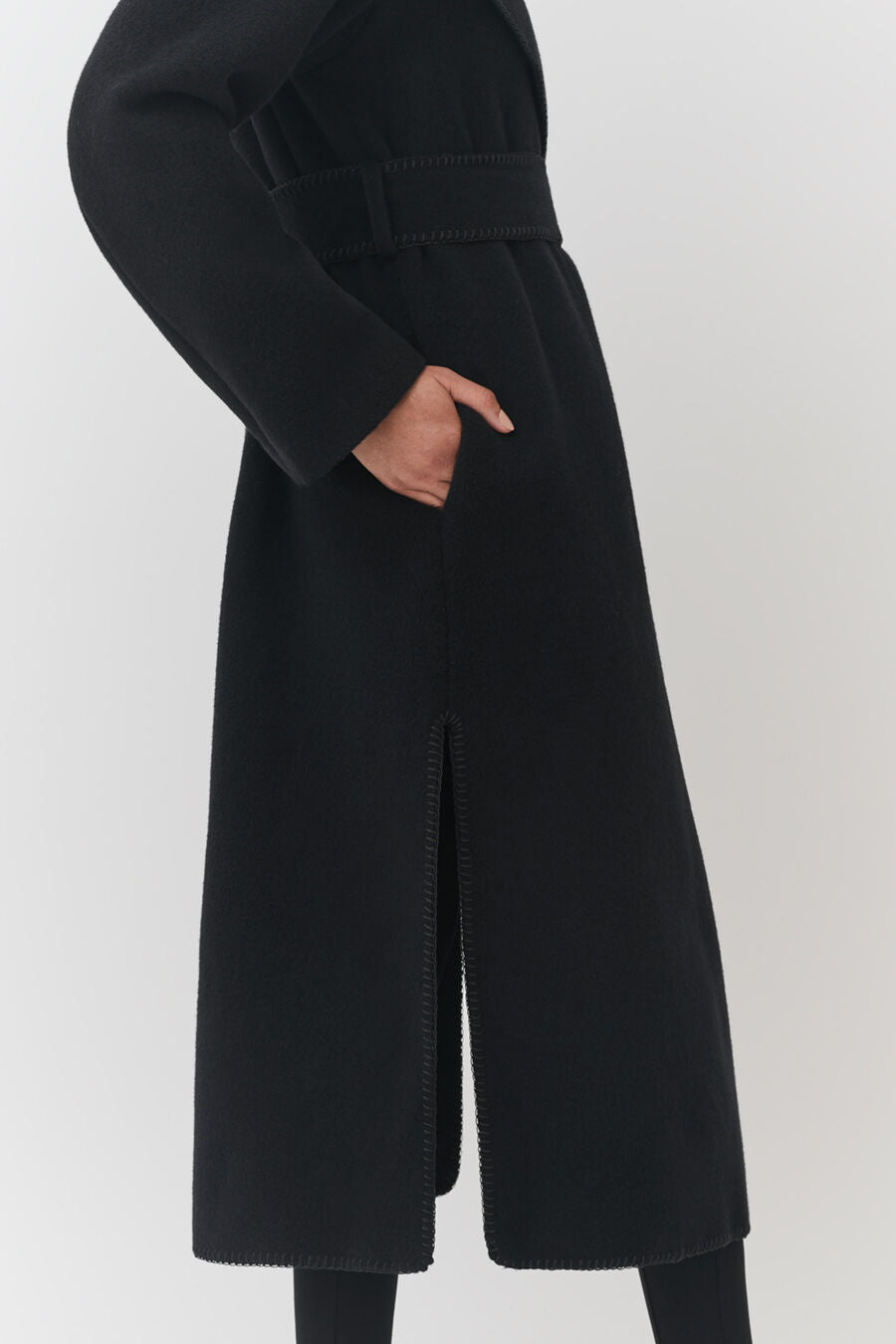 Person in a long coat with hand on hip, showing side zipper detail.
