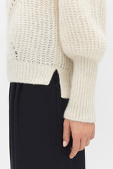 Close-up of a person wearing a sweater and pants, hand resting by their side.