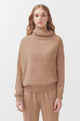 Woman in turtleneck sweater and matching pants standing indoors.