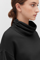 Side profile of a woman wearing a high-neck top with hair in a bun.