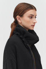 Profile view of a woman with a ponytail wearing a jacket with a high collar.
