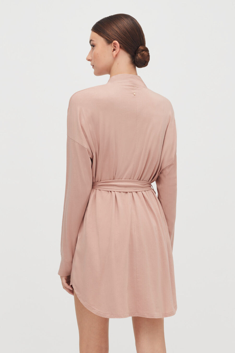 Woman facing away, wearing a dress with long sleeves and a tied belt at the waist.