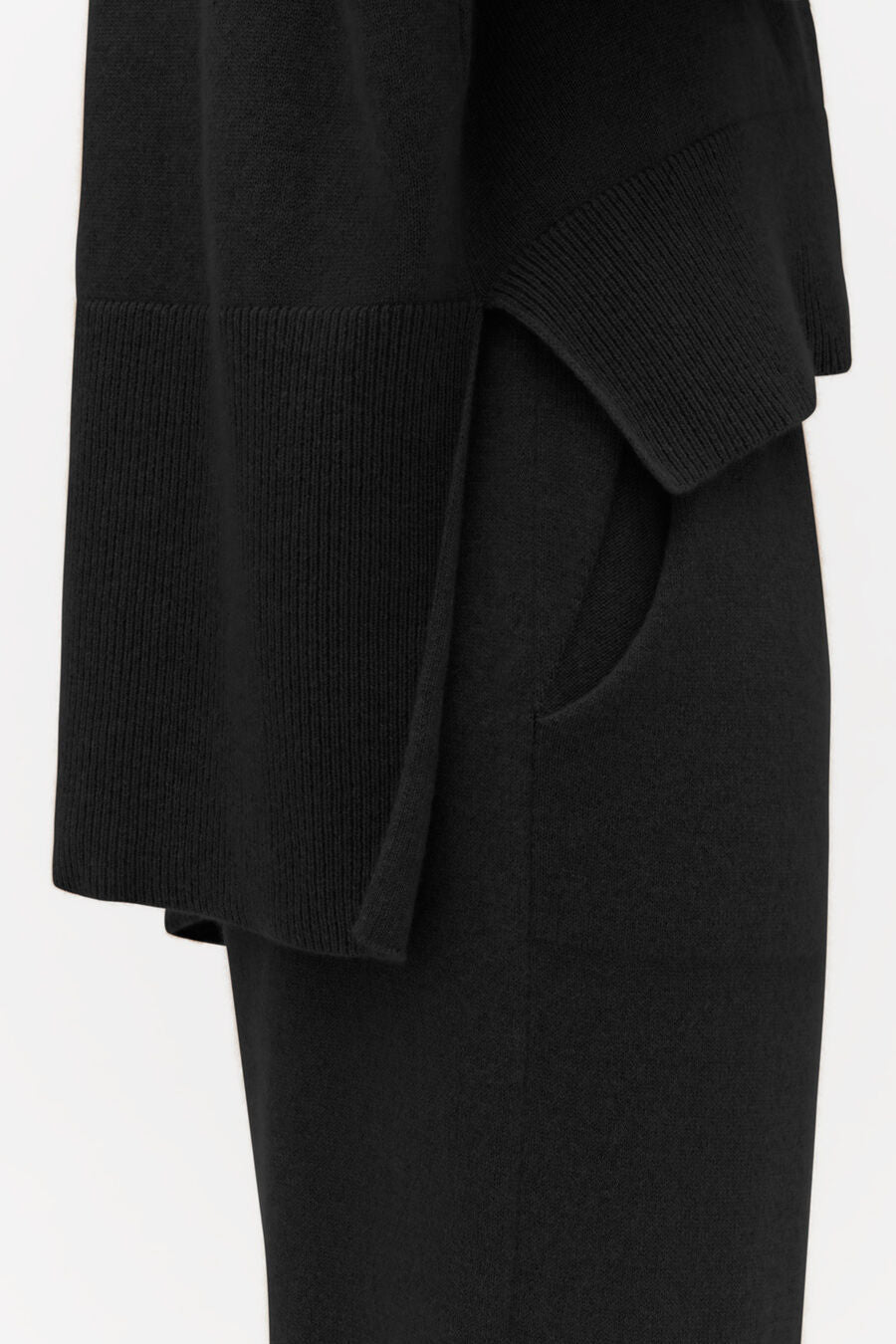 Close-up of a sweater with ribbed cuffs and a coat over trousers.
