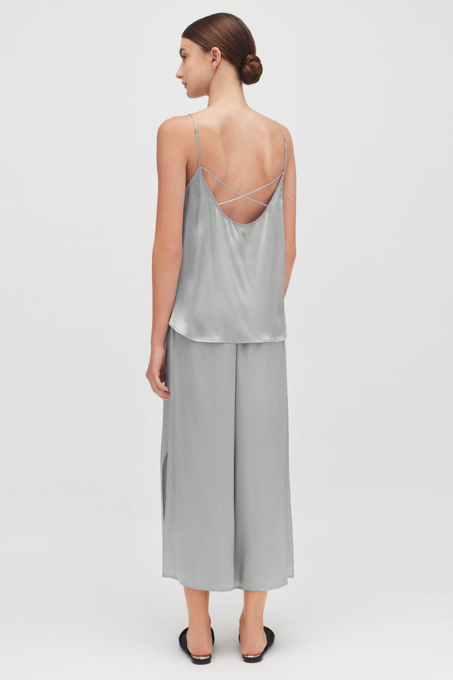 Woman standing, viewed from behind, wearing a sleeveless top and pants.