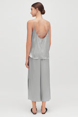 Woman standing, viewed from behind, wearing a sleeveless top and pants.