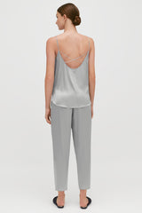 Woman standing facing away wearing a top with criss-cross back straps and pants.