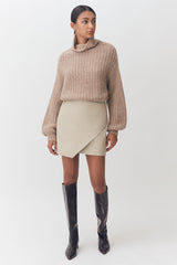 Woman in a turtleneck and skirt with knee-high boots standing.