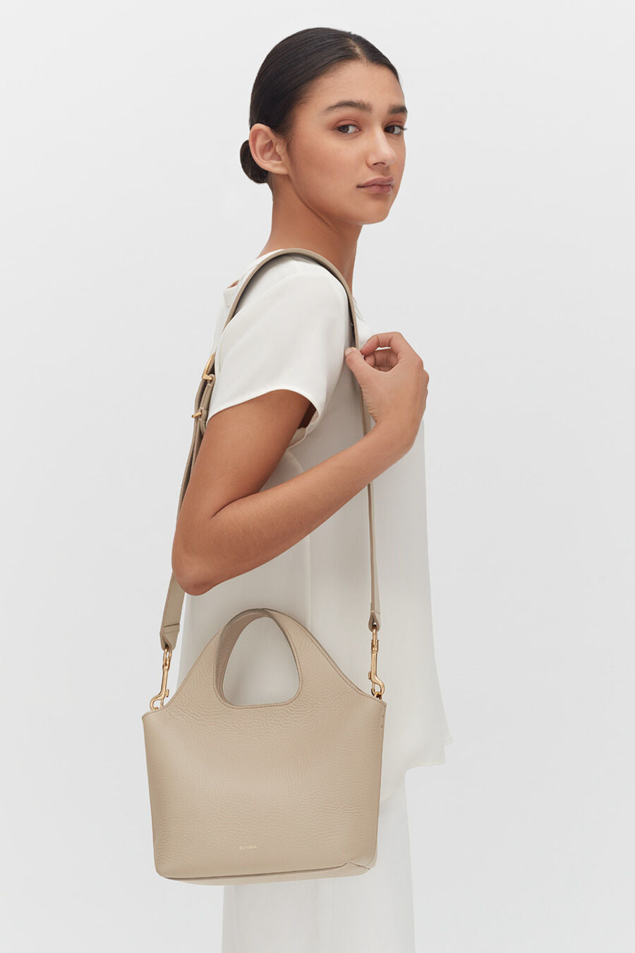 Woman standing with a shoulder bag, looking over her shoulder.