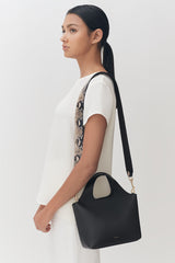 Woman standing in profile wearing a dress and carrying a shoulder bag.