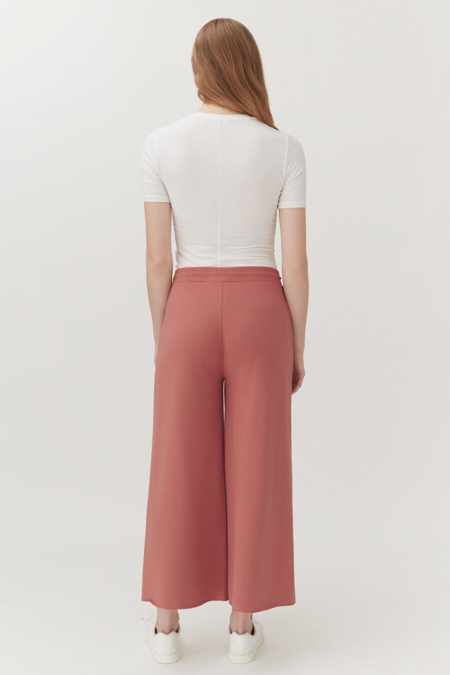 Woman viewed from behind wearing a fitted top and wide-leg pants, standing.