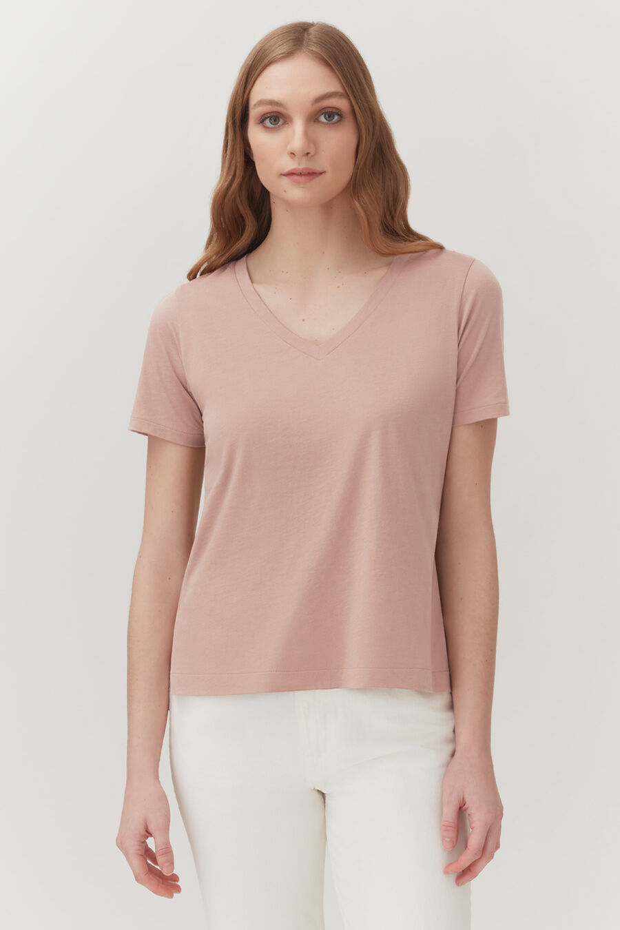 Woman in a V-neck T-shirt and pants standing against a plain background.