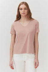 Woman in a V-neck T-shirt and pants standing against a plain background.