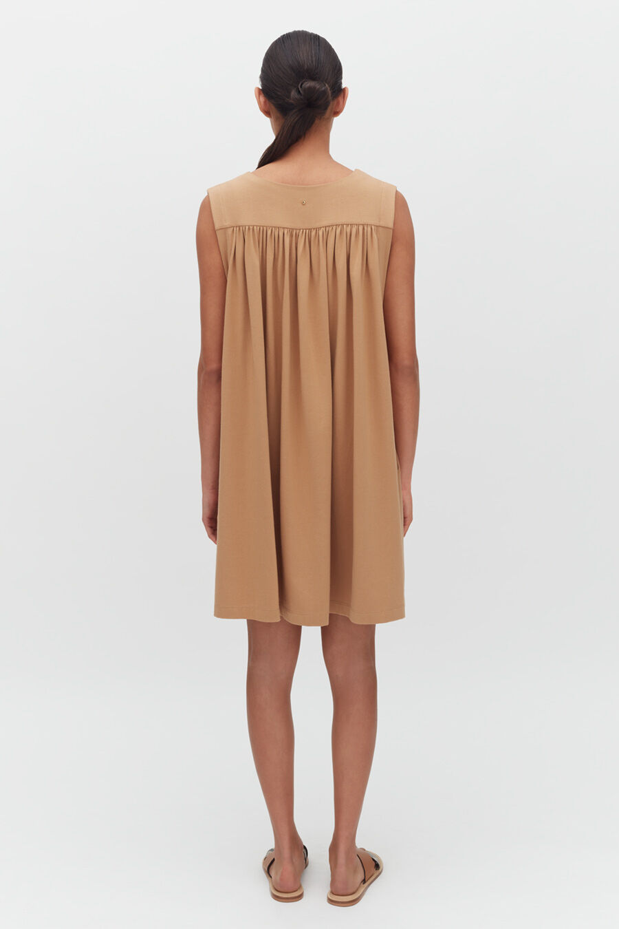 Woman standing, viewed from behind, wearing a knee-length dress and sandals.