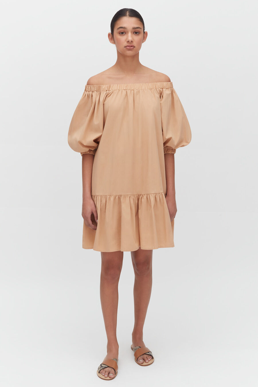 Woman standing in a puffy-sleeved off-shoulder dress with sandals.