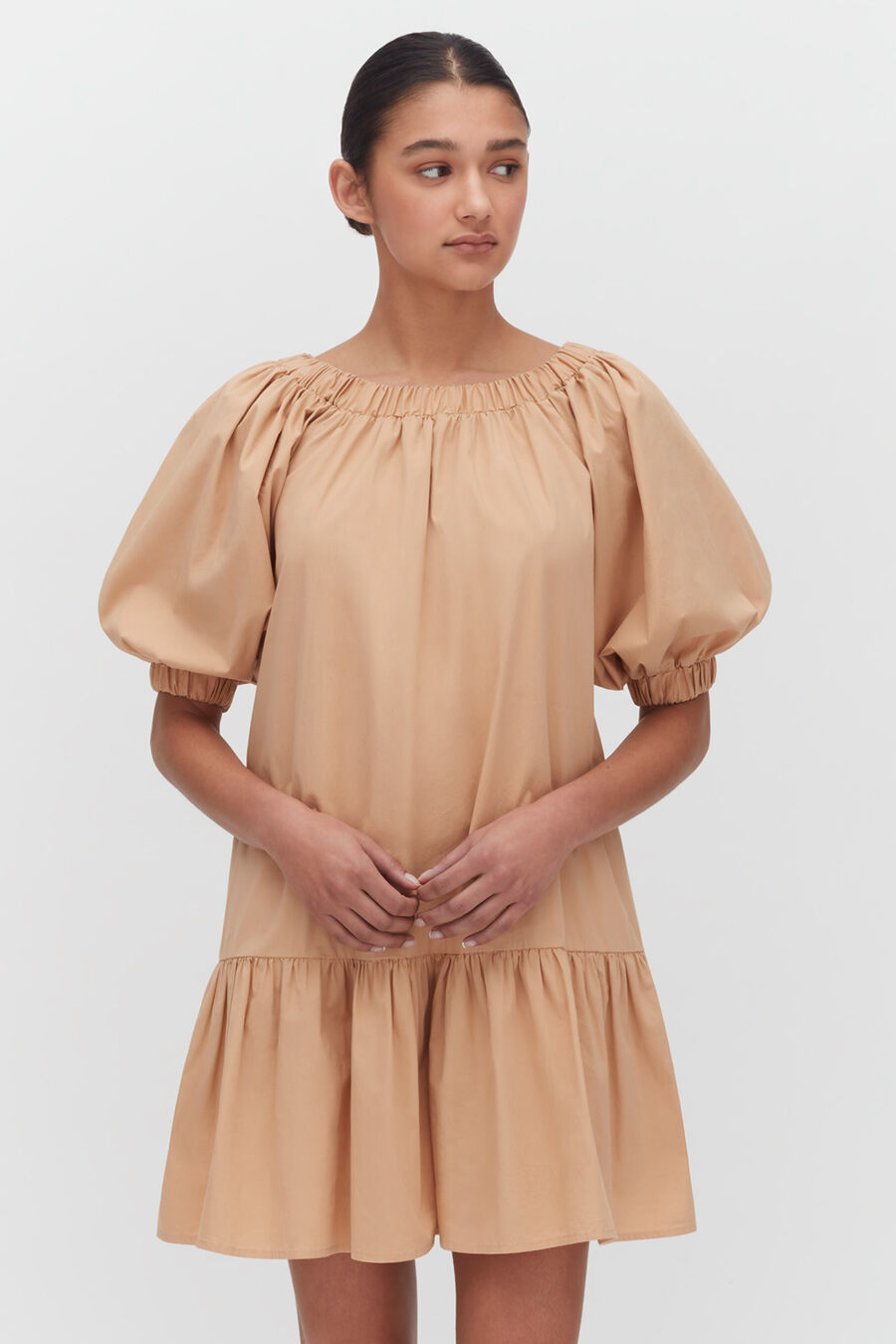 Woman posing in a short dress with puffy sleeves and gathered neckline.