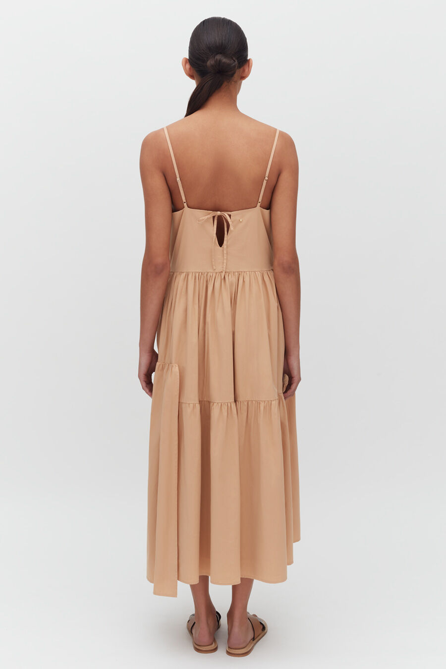 Woman from behind wearing a sleeveless, knee-length dress standing upright.