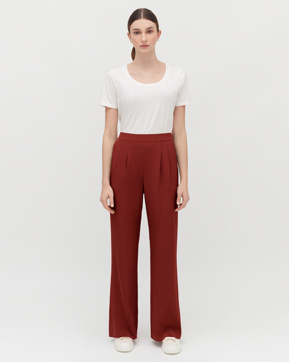 Woman standing in a white shirt and wide-legged pants against a neutral background.