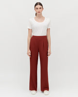 Woman standing in a white shirt and wide-legged pants against a neutral background.