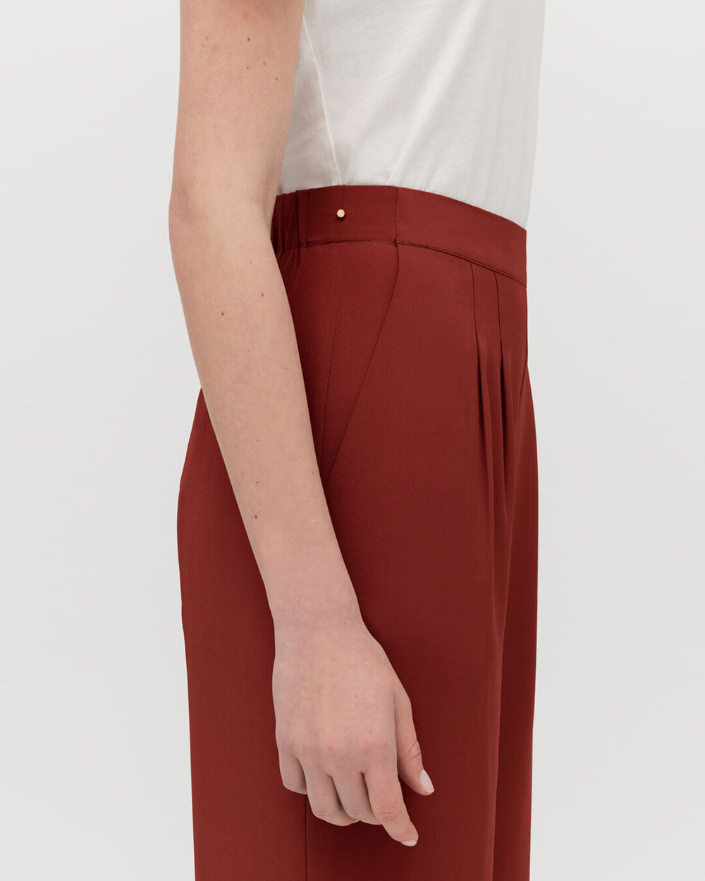 Person standing in high-waisted trousers, close-up of waist and arm.
