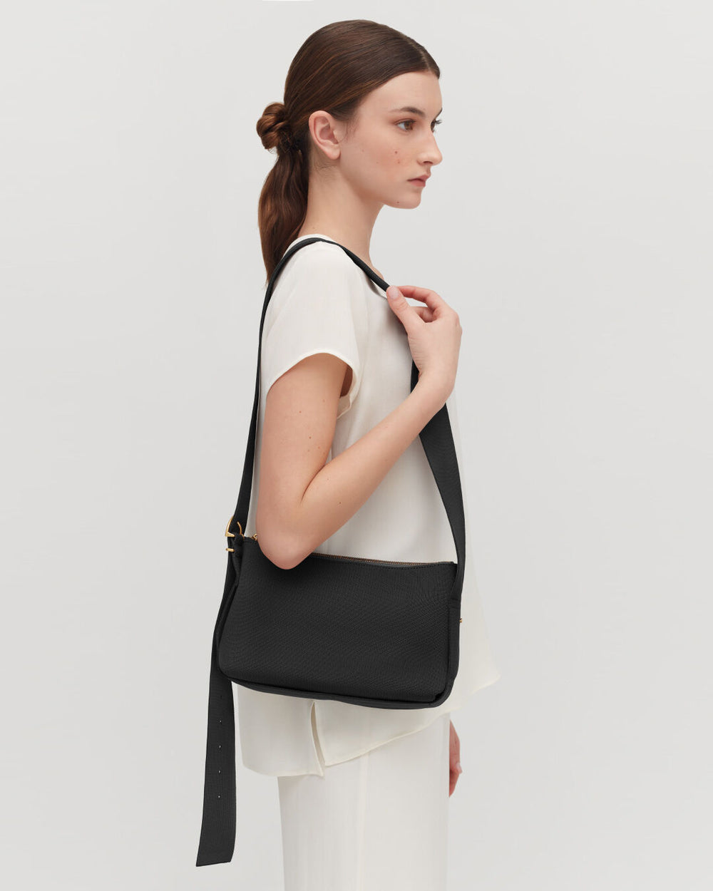 Woman standing sideways with a handbag over her shoulder.