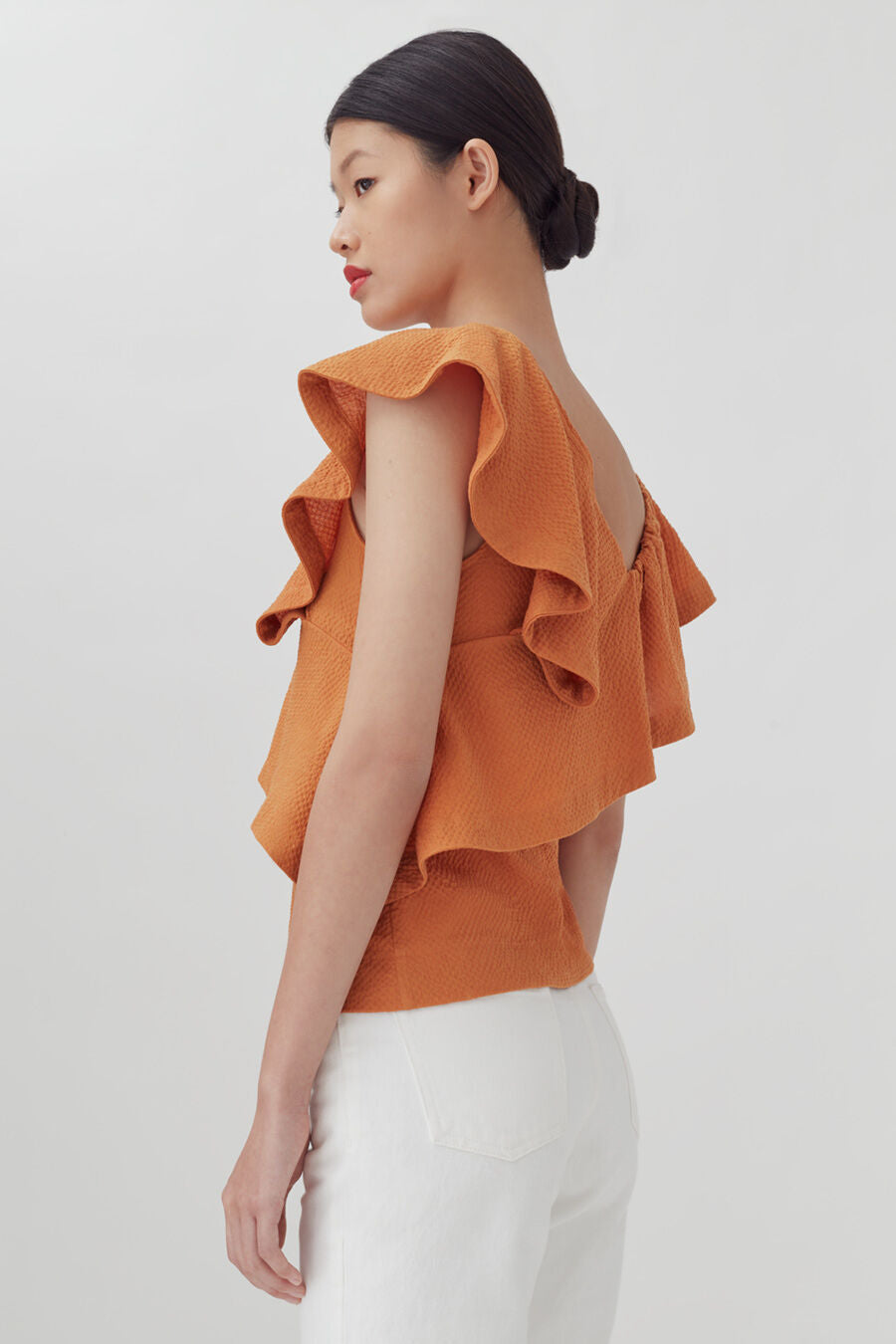 Woman in a ruffled top, viewed from the side.