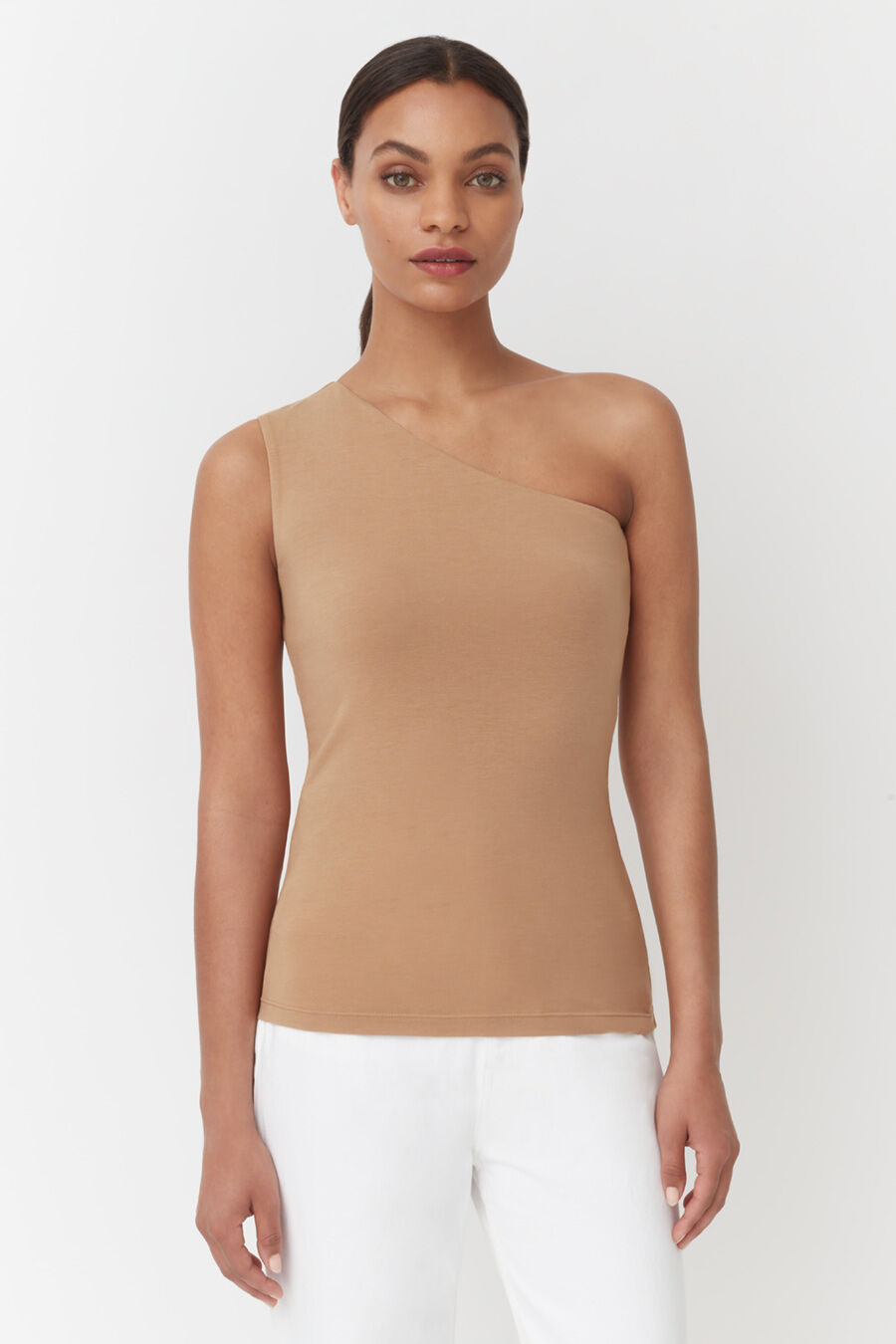 Woman wearing a one-shoulder top and white pants standing straight