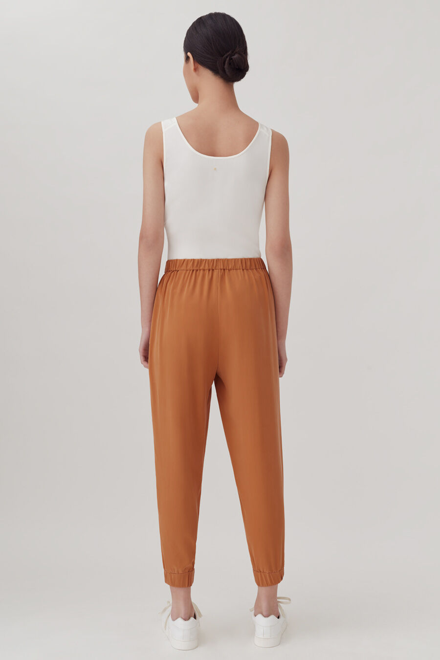 Woman standing with back to camera, wearing a sleeveless top and pants.