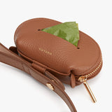 Small oval purse with strap and a green leaf peeking out.
