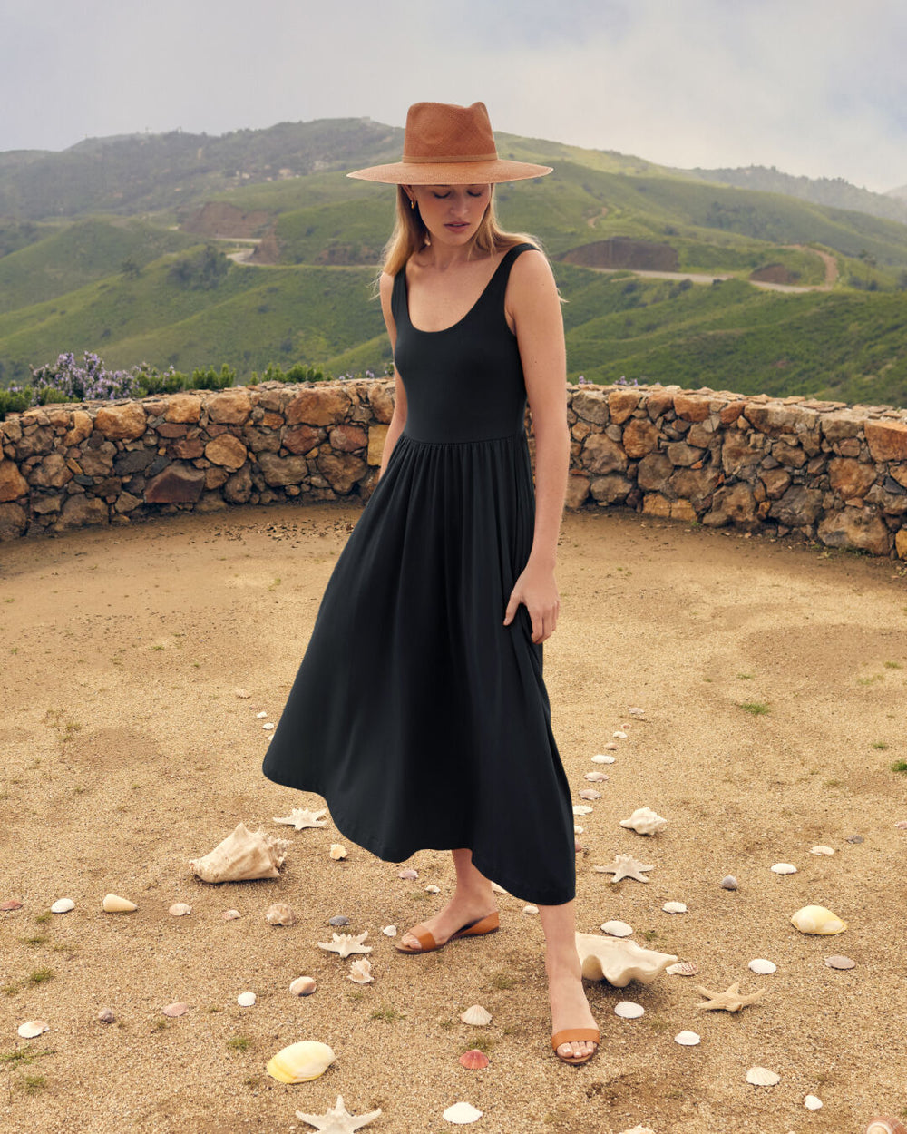 Woman in a dress and hat standing outdoors with scattered shells around her.