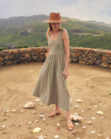 Woman in a dress and hat standing outdoors with scattered objects around her.