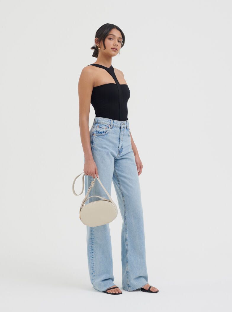 Woman standing with handbag, wearing a sleeveless top and jeans.